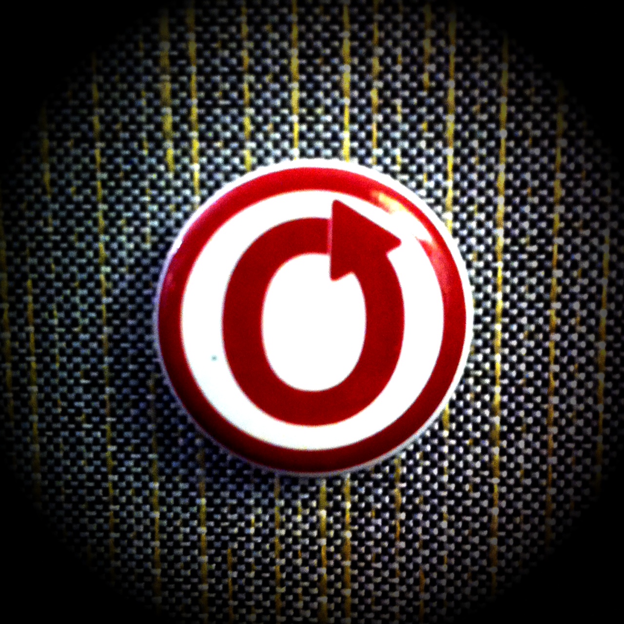 Color photo of OTW logo button against a cloth field.
