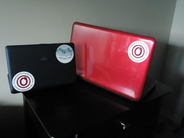Color photo of one black laptop and one red laptop with OTW stickers on the covers.