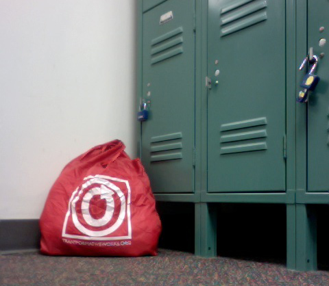 Color photo of OTW nylon carryall sitting in a corner on the floor in front of a bank of small lockers.